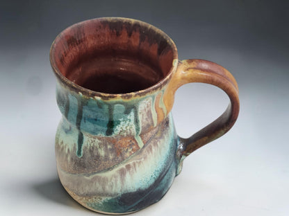 Handmade ceramic mug with glossy red brown interior and layered ash glaze exterior