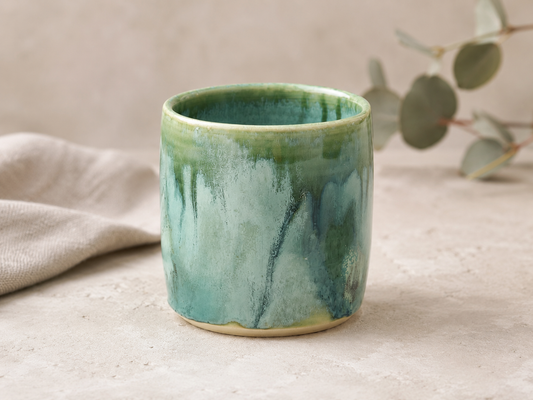 Handmade ceramic tumbler in Bush Creek Mist glaze styled with soft eucalyptus tones and natural linen