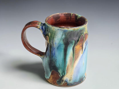 Handcrafted pottery mug featuring turquoise, forest green and ochre glaze.