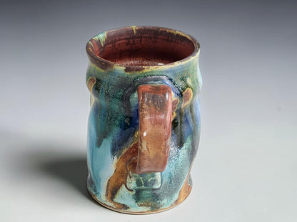 Colourful handmade pottery mug styled for morning coffee on a timber bench.