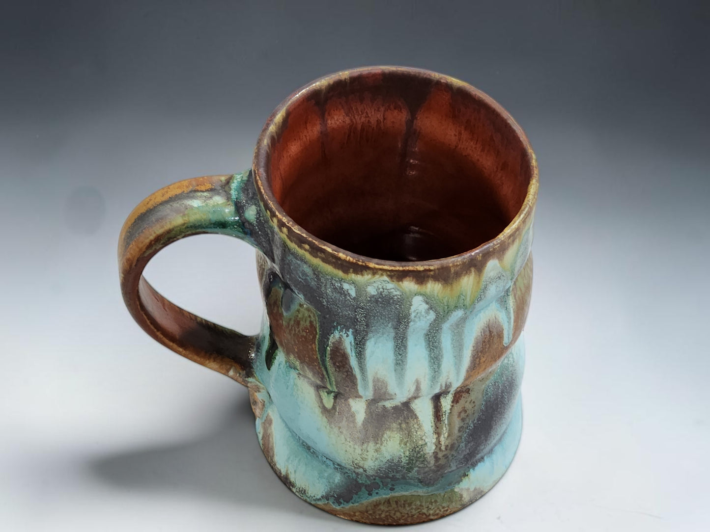Handmade stoneware mug with flowing ash glaze drips and glossy red brown glazed interior