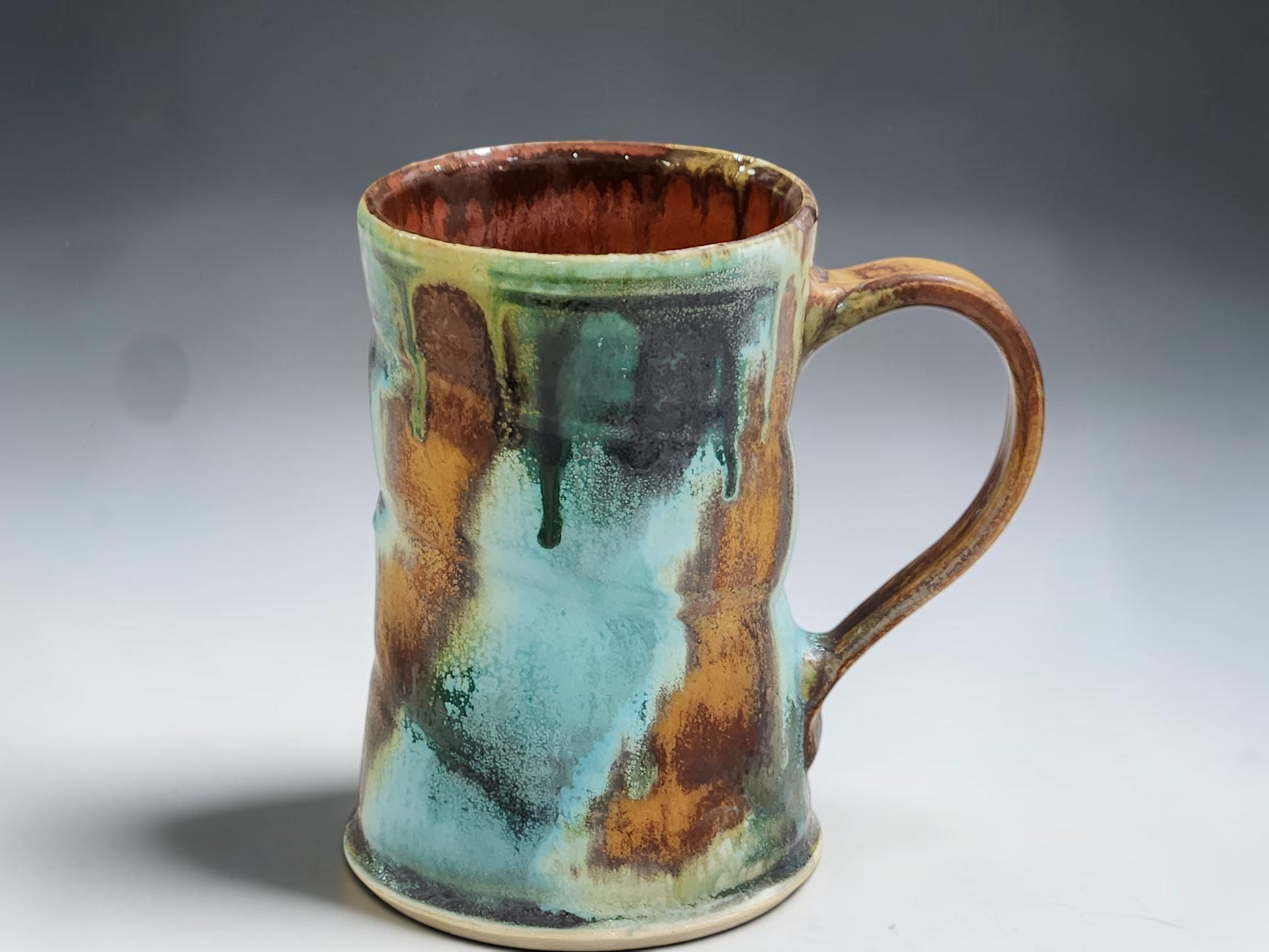 handmade ceramic mug showing turquoise, rust, brown and ash glaze drips with glossy red brown interior