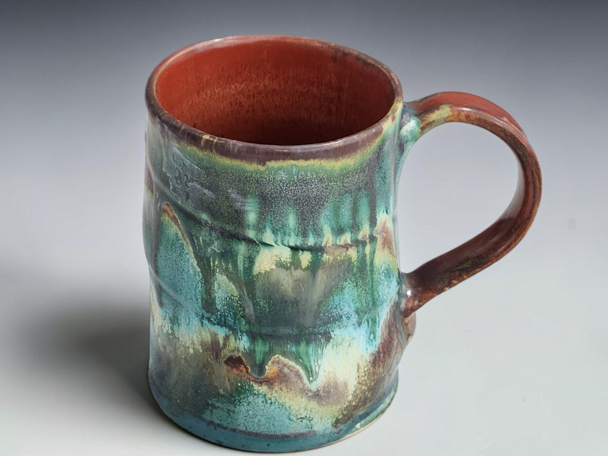 Handcrafted ceramic mug with a curved brown handle and rust-red interior.