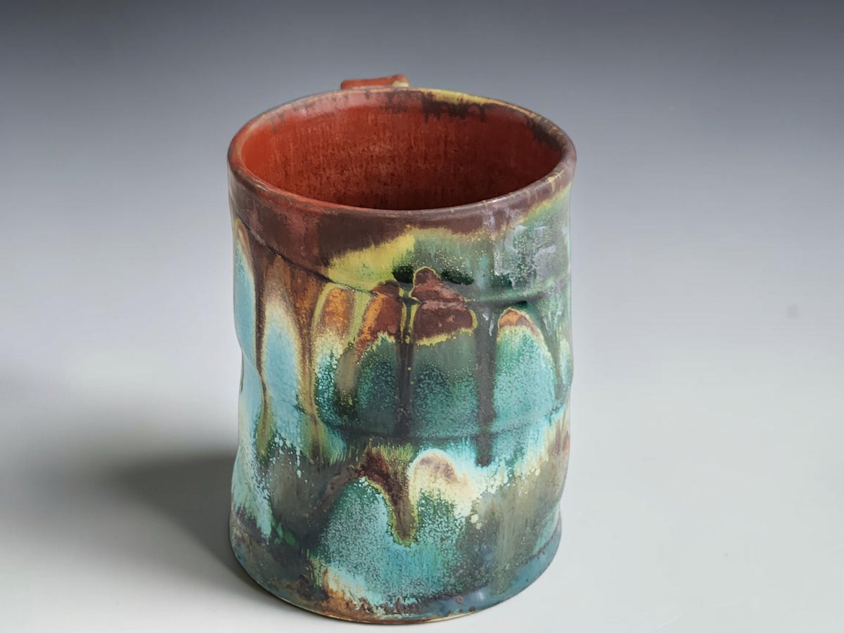 Turquoise and earthy brown pottery mug with a gently irregular dark rim.