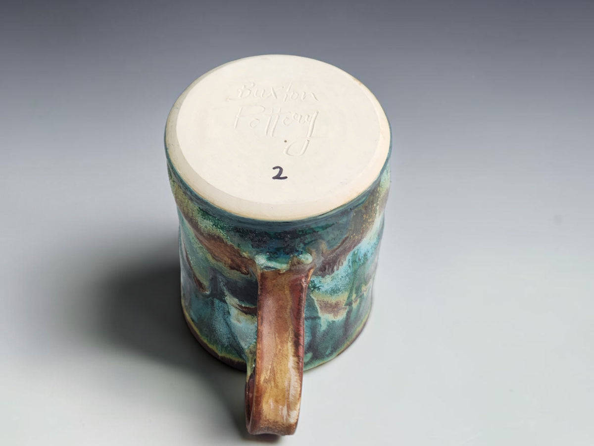 Green and turquoise pottery mug showing its underside and makers mark and rounded handle