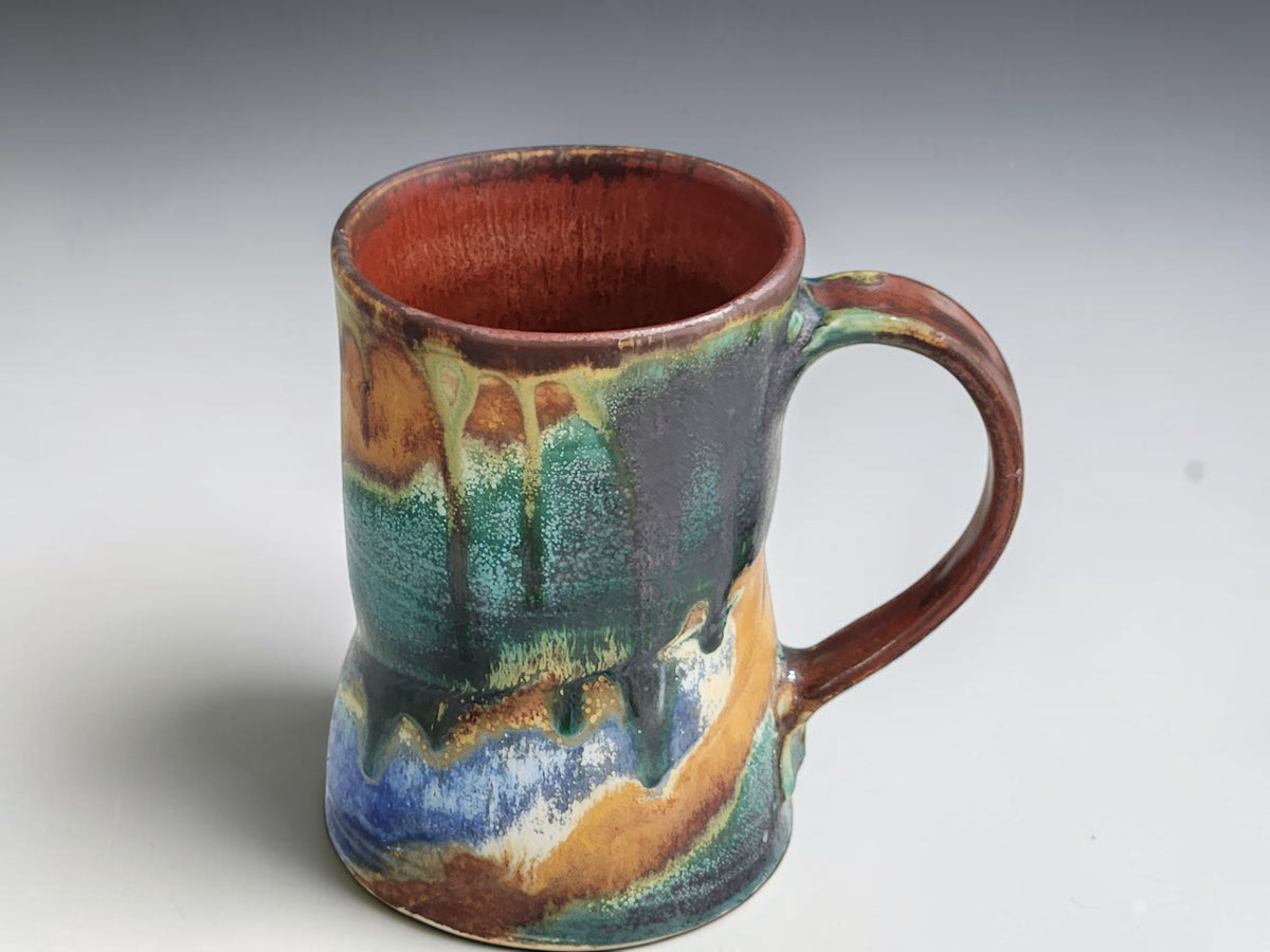 Tall ceramic mug with flowing green glaze drips over warm ochre brown.
