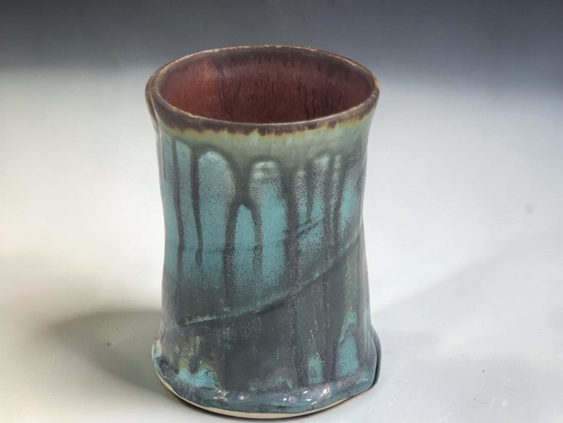 Handmade ceramic mug with ergonomic handle and flowing green-blue glaze, artisan pottery by Buxton Pottery.