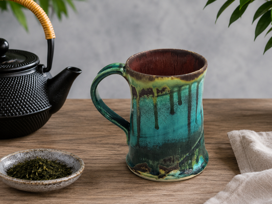 Handmade Bush Creek Earth pottery mug on a timber table with teapot and tea leaves, Australian ceramic coffee mug by Buxton Pottery.