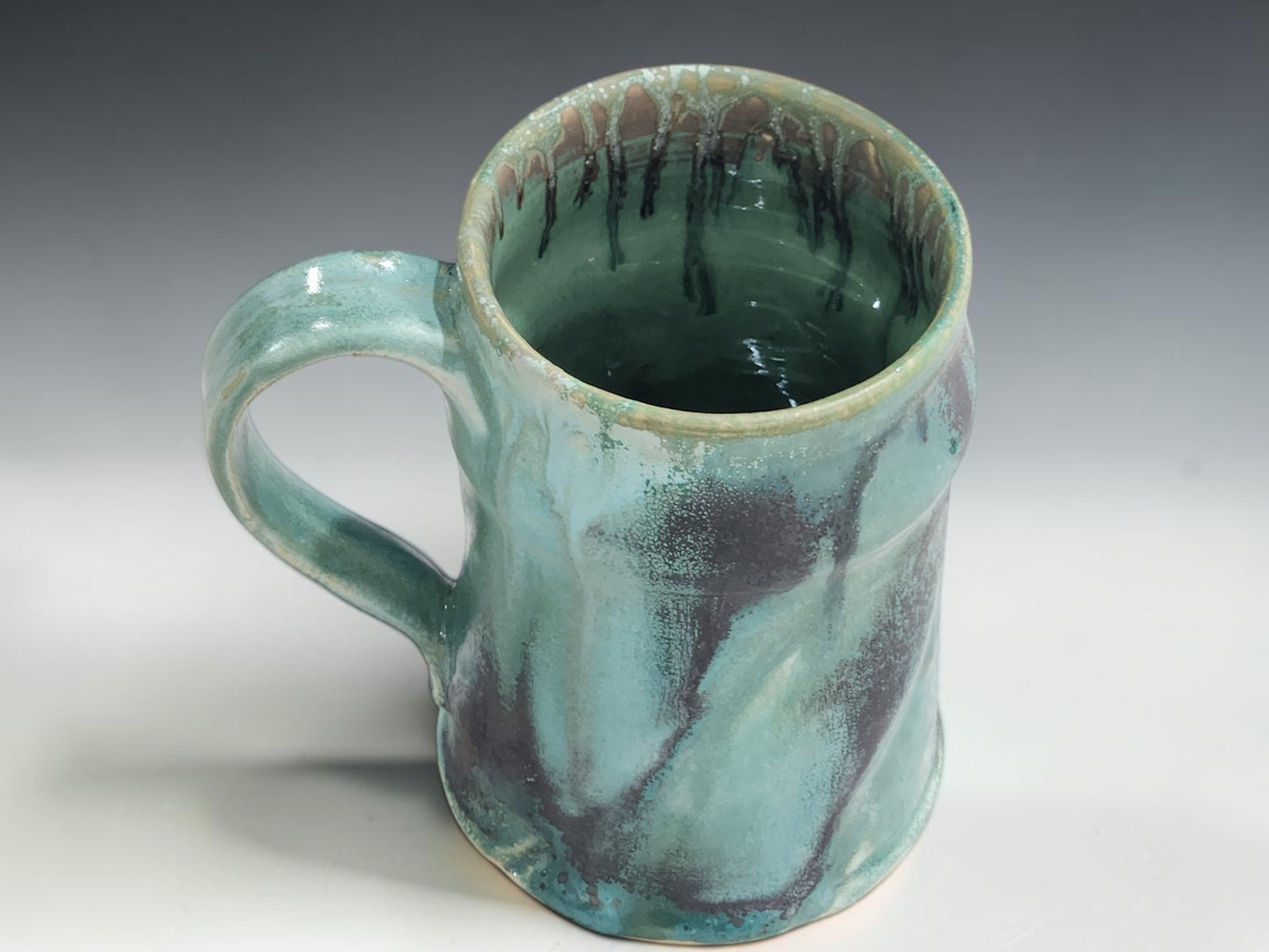 Wheel-thrown pottery mug with 350ml capacity, curved handle and glossy turquoise glaze on grey studio background