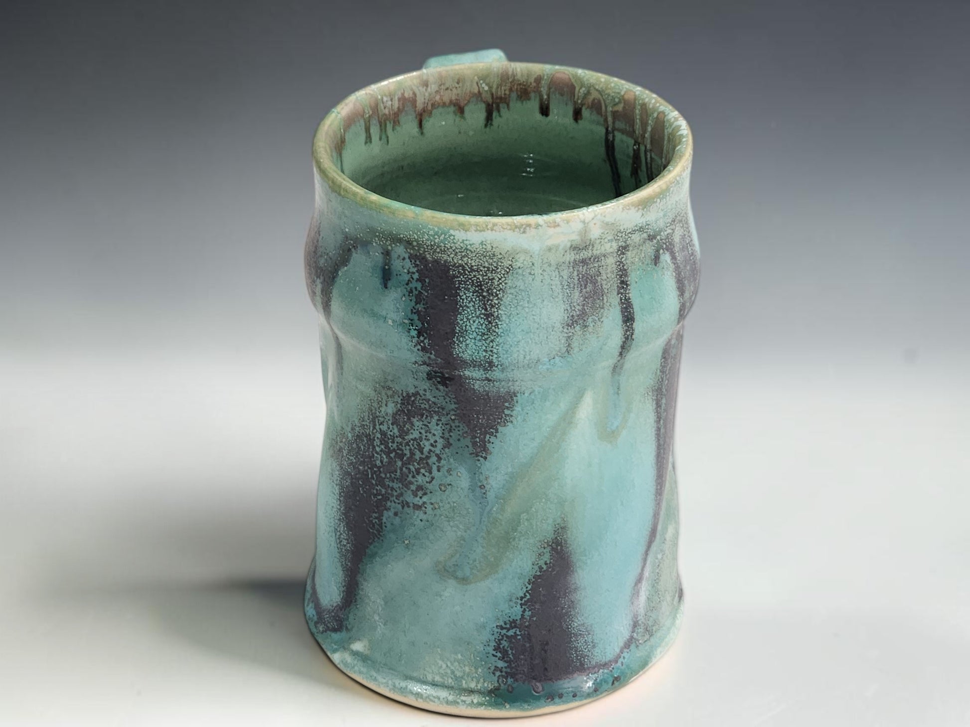 Handmade ceramic tea or coffee mug in green blue glaze, photographed on a neutral grey studio sweep