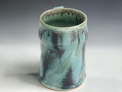 Handmade ceramic tea or coffee mug in green blue glaze, photographed on a neutral grey studio sweep
