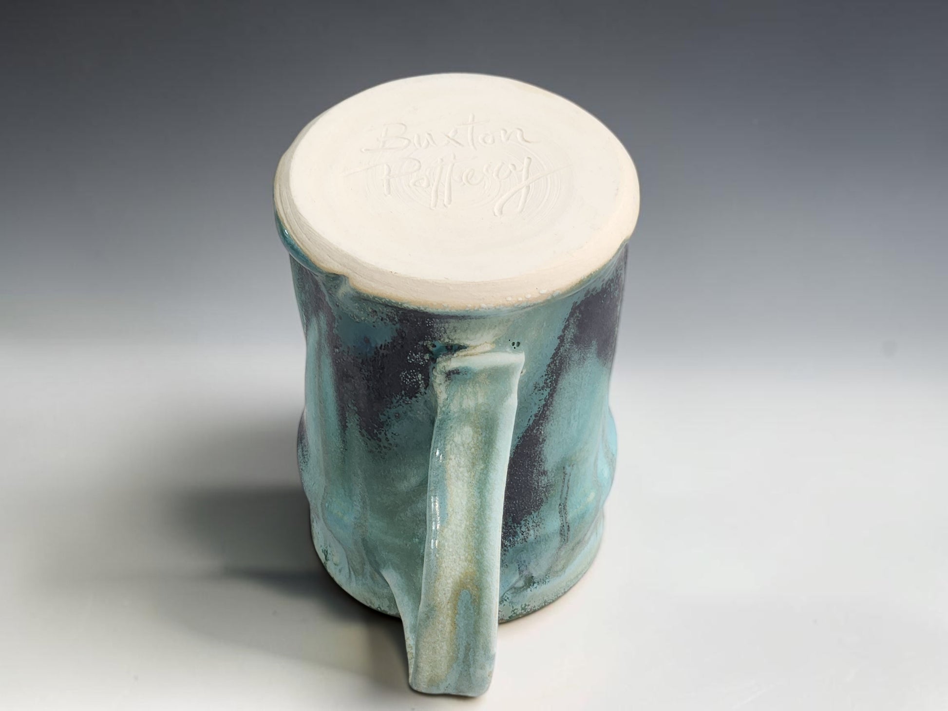 Handmade ceramic mug with curved handle, glossy flowing glaze and natural handmade variation on grey background