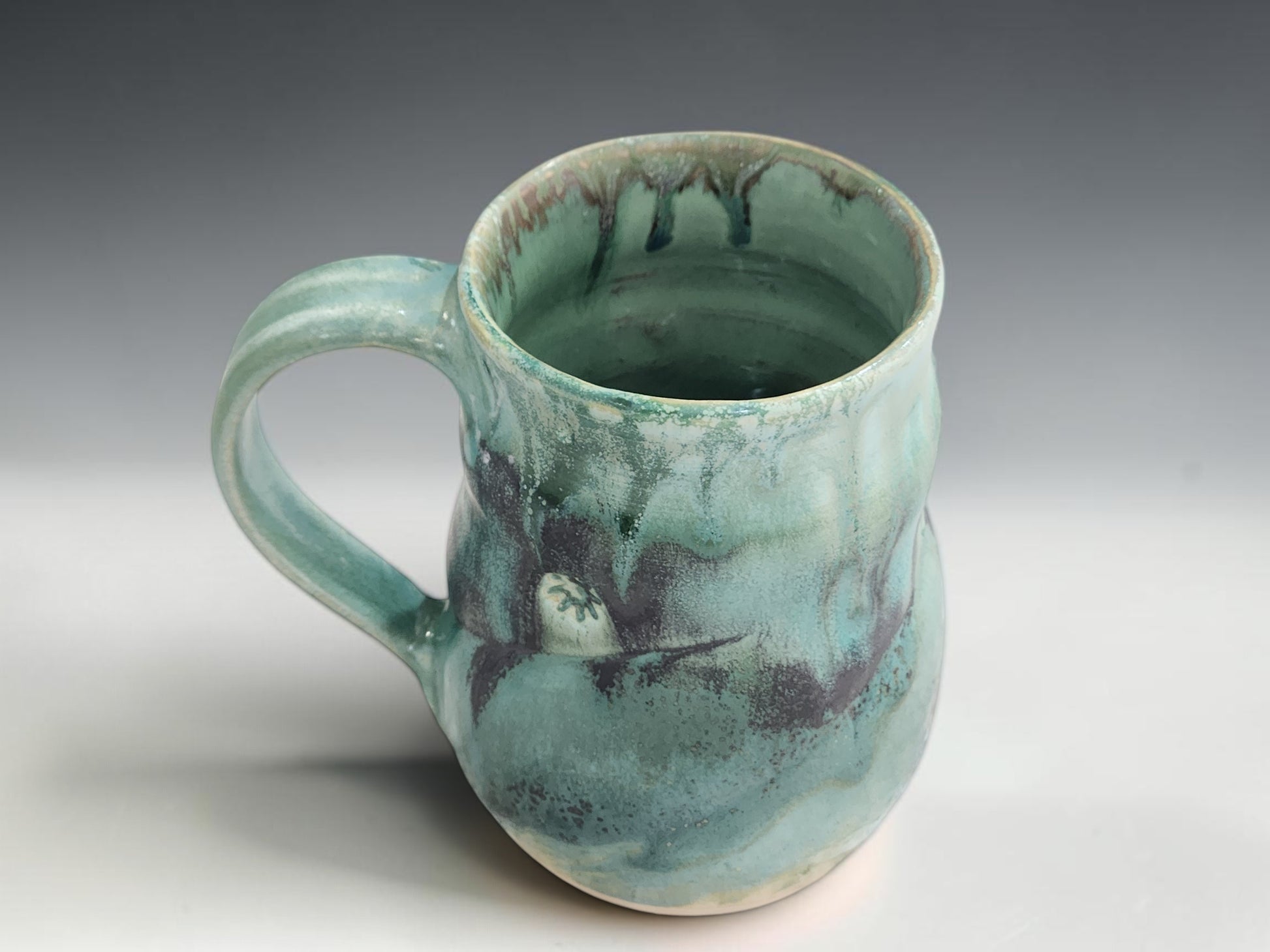 Wheel-thrown pottery mug with 450ml capacity, curved handle and glossy seafoam glaze on grey studio background
