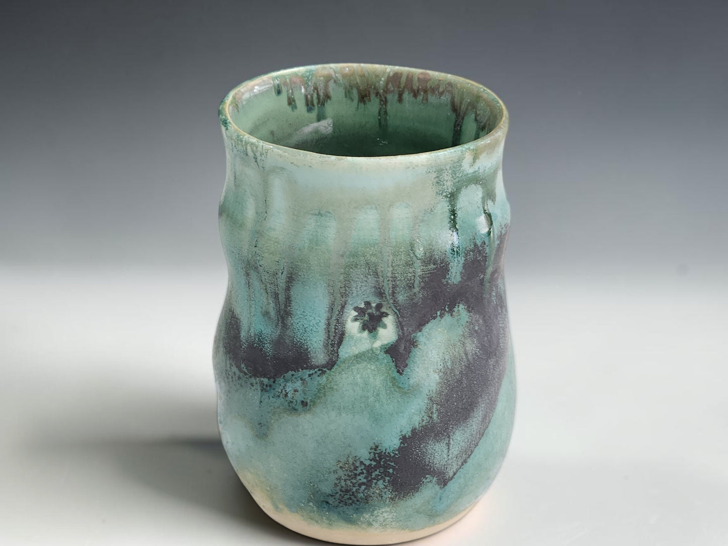 Handmade ceramic tea or coffee mug in green blue glaze, photographed on a neutral grey studio sweep