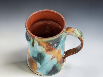 Handmade ceramic coffee mug in turquoise, rust brown and moss green glaze, photographed on a neutral grey studio sweep