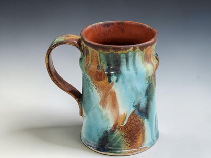 Rustic handmade stoneware mug with warm terracotta interior and flowing aqua green exterior glaze