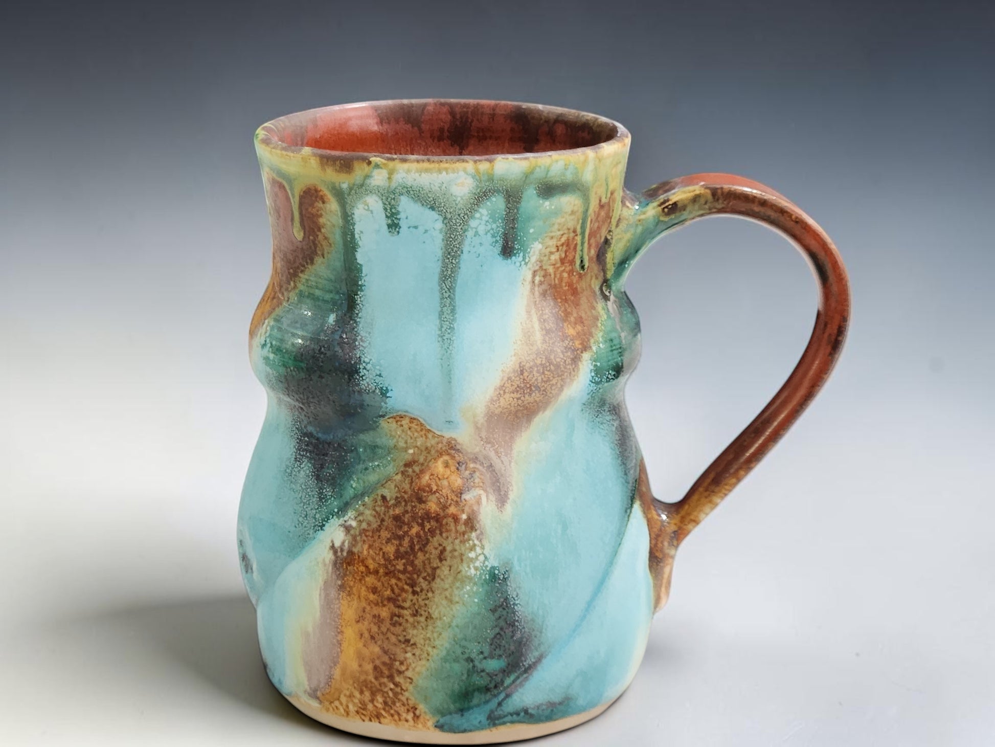 Rustic handmade stoneware mug with warm terracotta interior and flowing aqua green exterior glaze