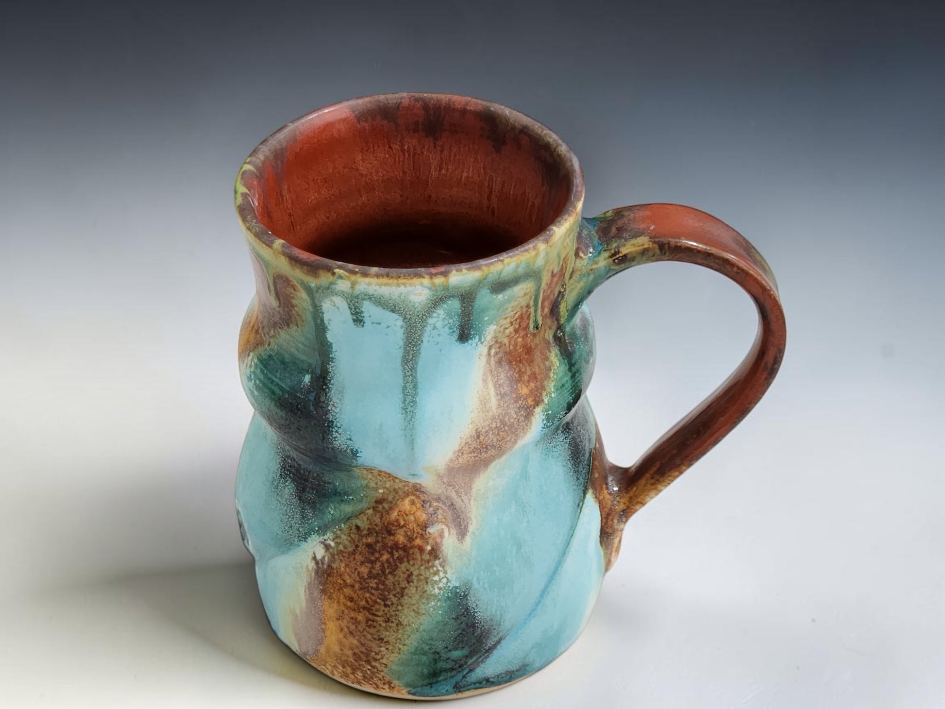 Close-up of handmade pottery mug showing turquoise, terracotta, green and deep earthy Bush Creek glaze movement
