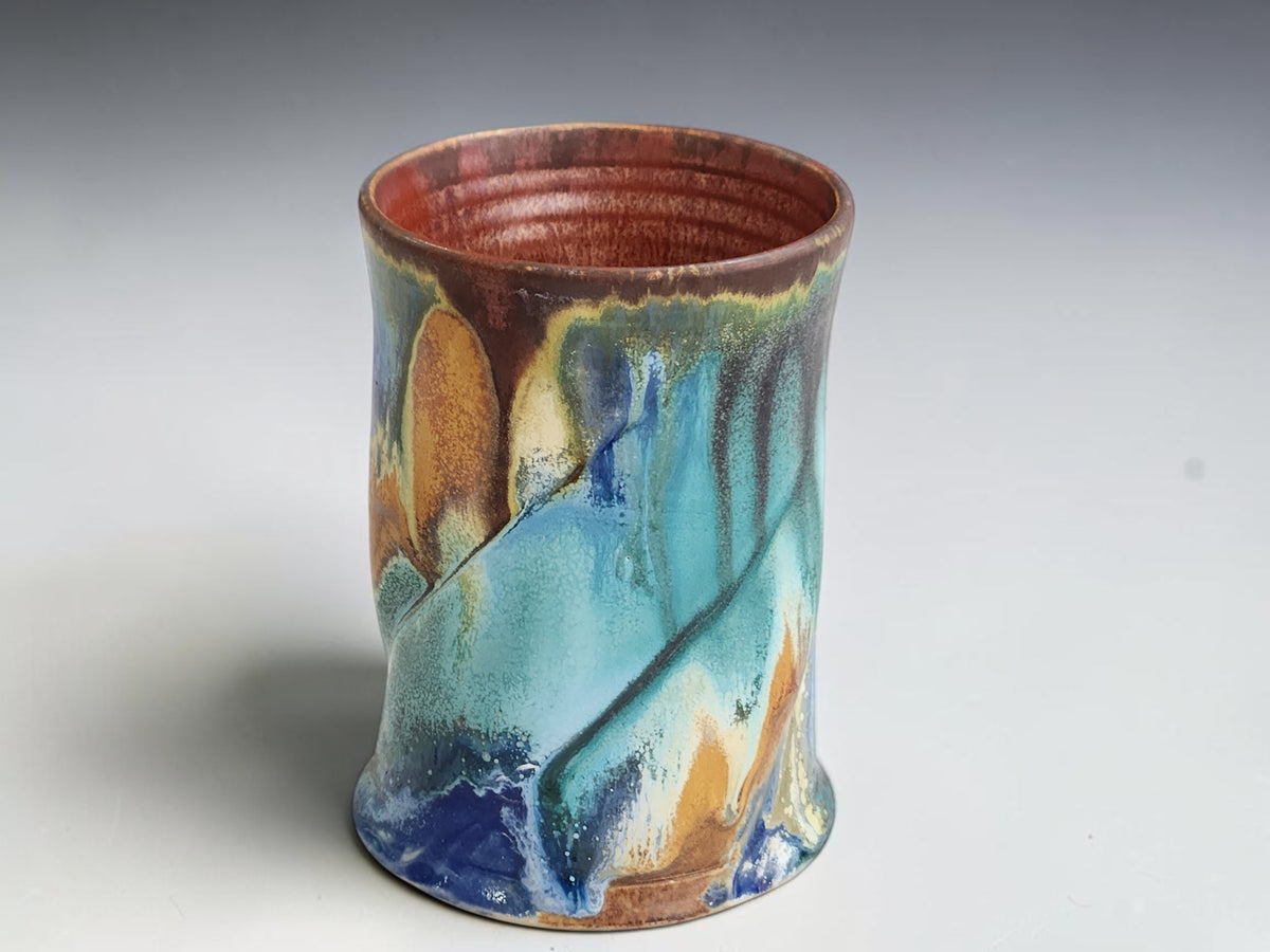 Front view of a handmade ceramic mug showing layered turquoise and earthy glaze details.