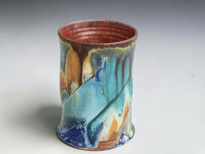 Front view of a handmade ceramic mug showing layered turquoise and earthy glaze details.