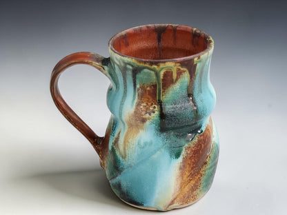 Handmade ceramic coffee mug in turquoise, earthy brown and moss green glaze, photographed on a neutral grey studio sweep