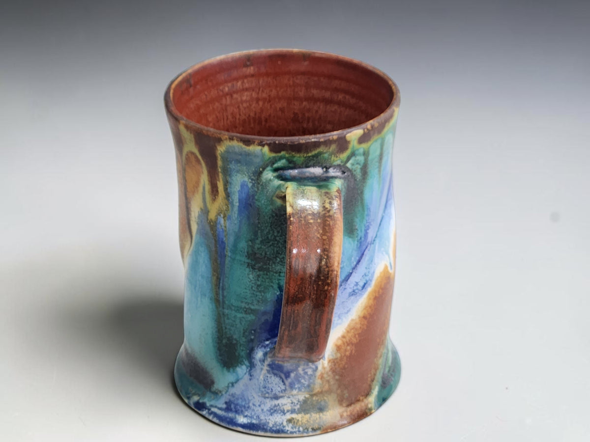 Turquoise pottery mug with a gently flared base and blue glaze accents around the foot.