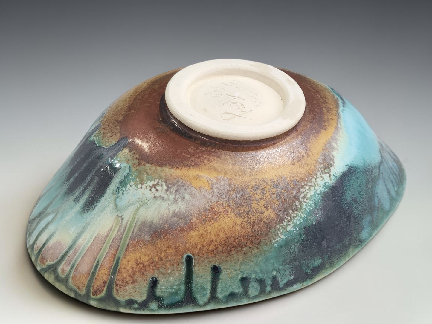 Handmade pottery bowl on grey studio background showing oval form, altered rim and Bush Creek glaze