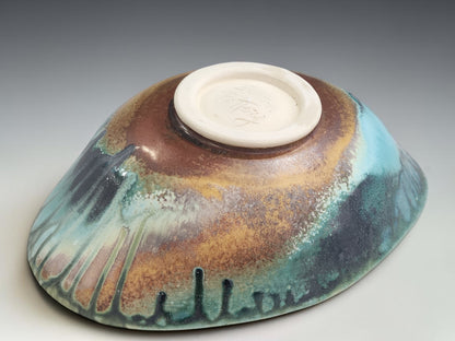 Handmade pottery bowl on grey studio background showing oval form, altered rim and Bush Creek glaze