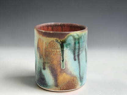 Small handmade pottery cup with earthy terracotta interior and layered turquoise green glaze