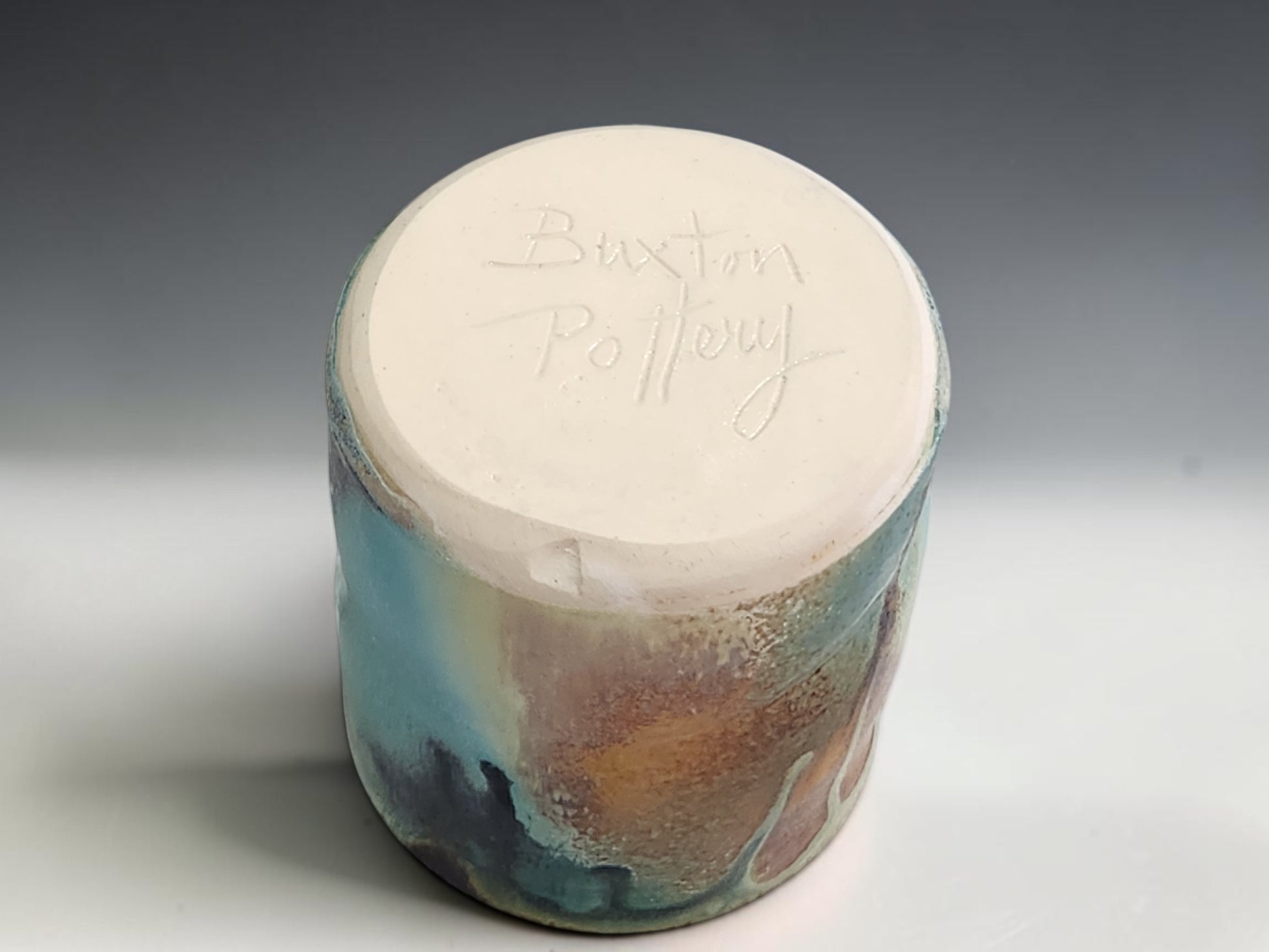 Handmade stoneware cup on grey studio background showing compact form and layered Bush Creek glaze