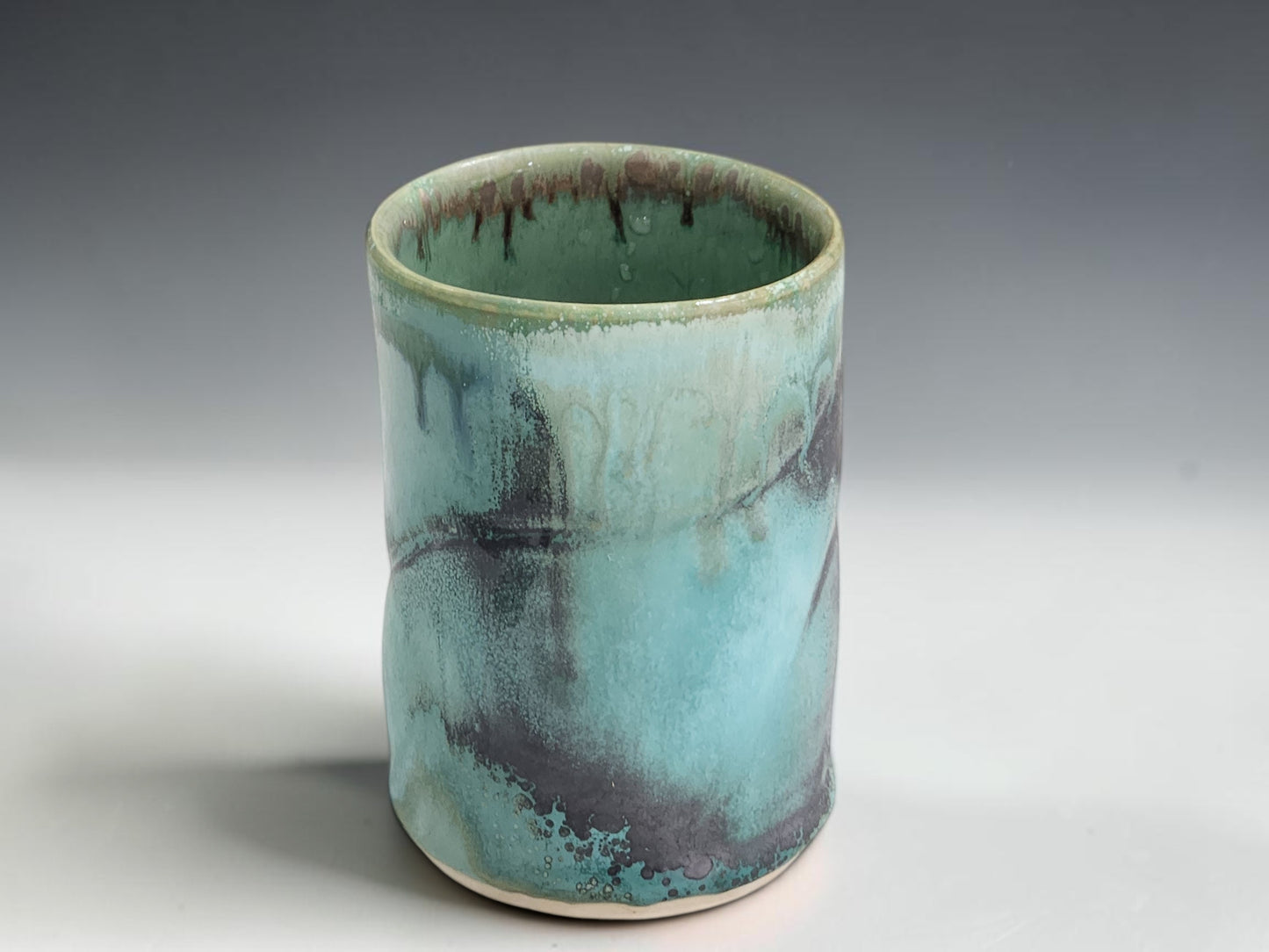 Small handmade pottery cup with straight-sided shape and organic green blue glaze variation