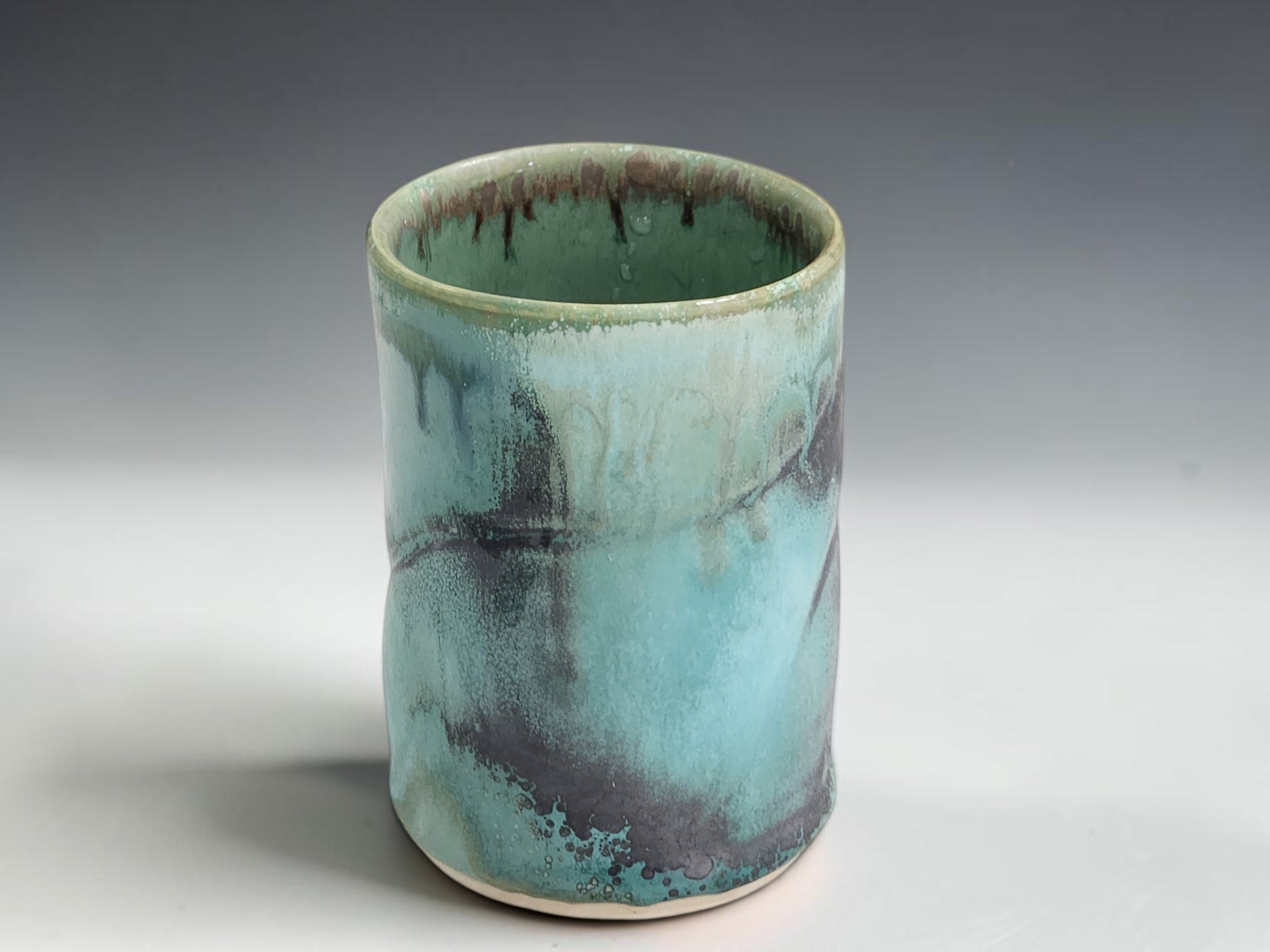 Small handmade pottery cup with straight-sided shape and organic green blue glaze variation