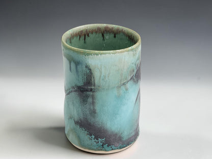 Small handmade pottery cup with straight-sided shape and organic green blue glaze variation