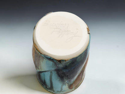 Handmade pottery tumbler on grey studio background showing tall form and layered Bush Creek glaze showing the bottom of the tumbler with the makers mark
