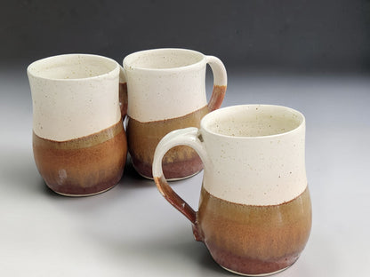 Three speckled cream and earthy brown pottery mugs displayed together, sold individually

