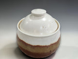Handmade ceramic sugar bowl with lid featuring cream and warm brown glaze, photographed on a professional studio sweep with a neutral grey gradient background.