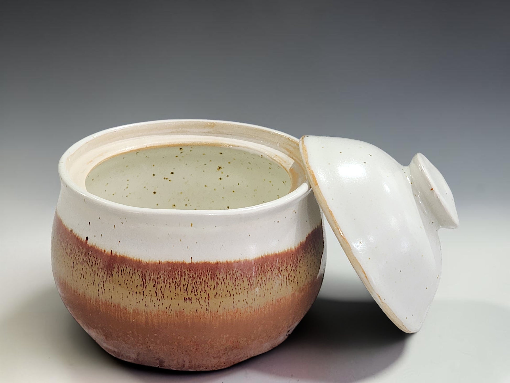 Wheel-thrown ceramic sugar container with matching lid and rustic glaze finish, photographed on a neutral grey gradient sweep for product presentation.