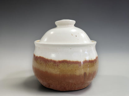 Cream and brown glazed ceramic sugar bowl with fitted lid, product image on a seamless neutral grey gradient background highlighting craftsmanship and form.