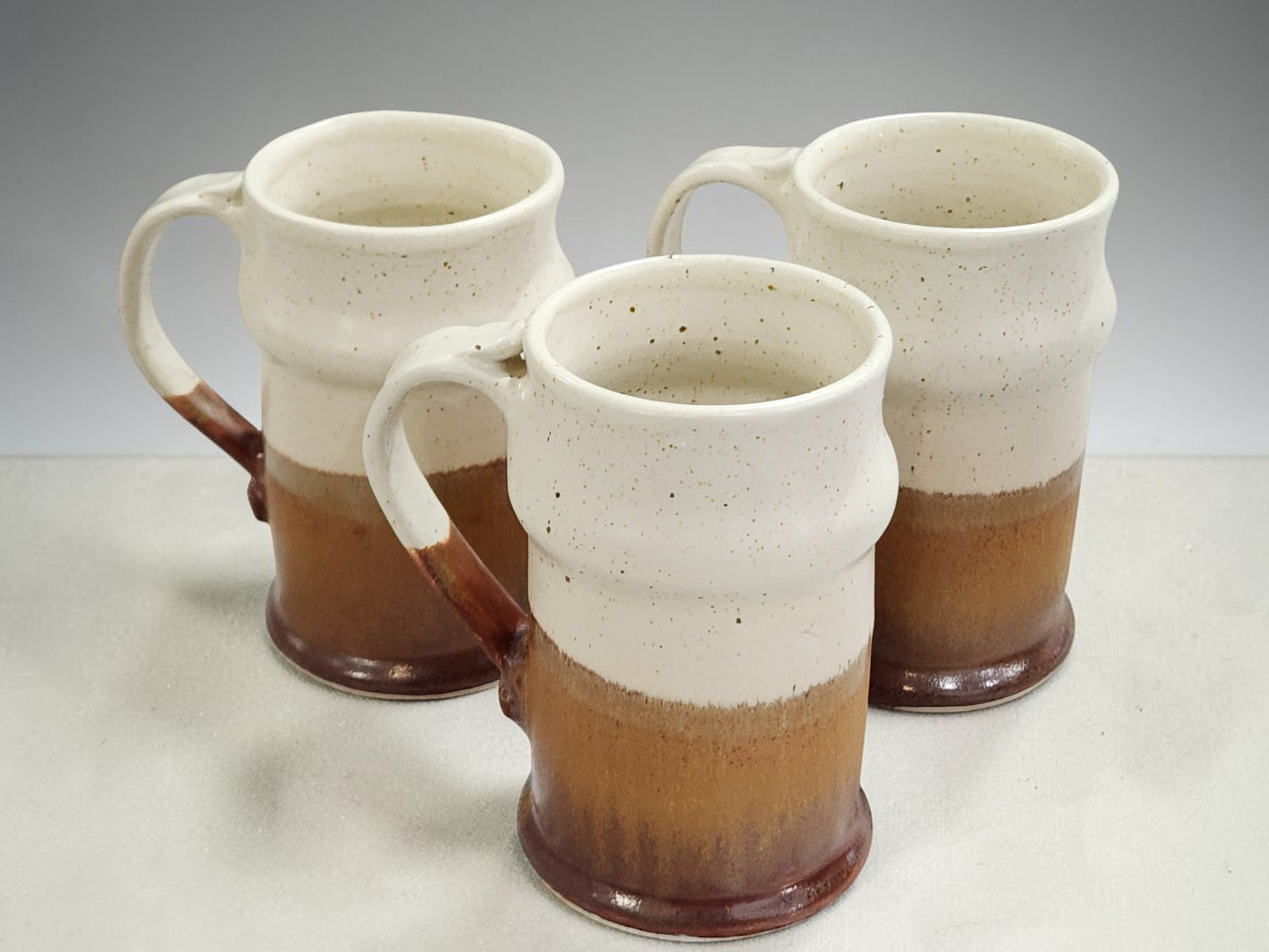 Set of three tall handmade pottery steins with speckled glaze and curved handles