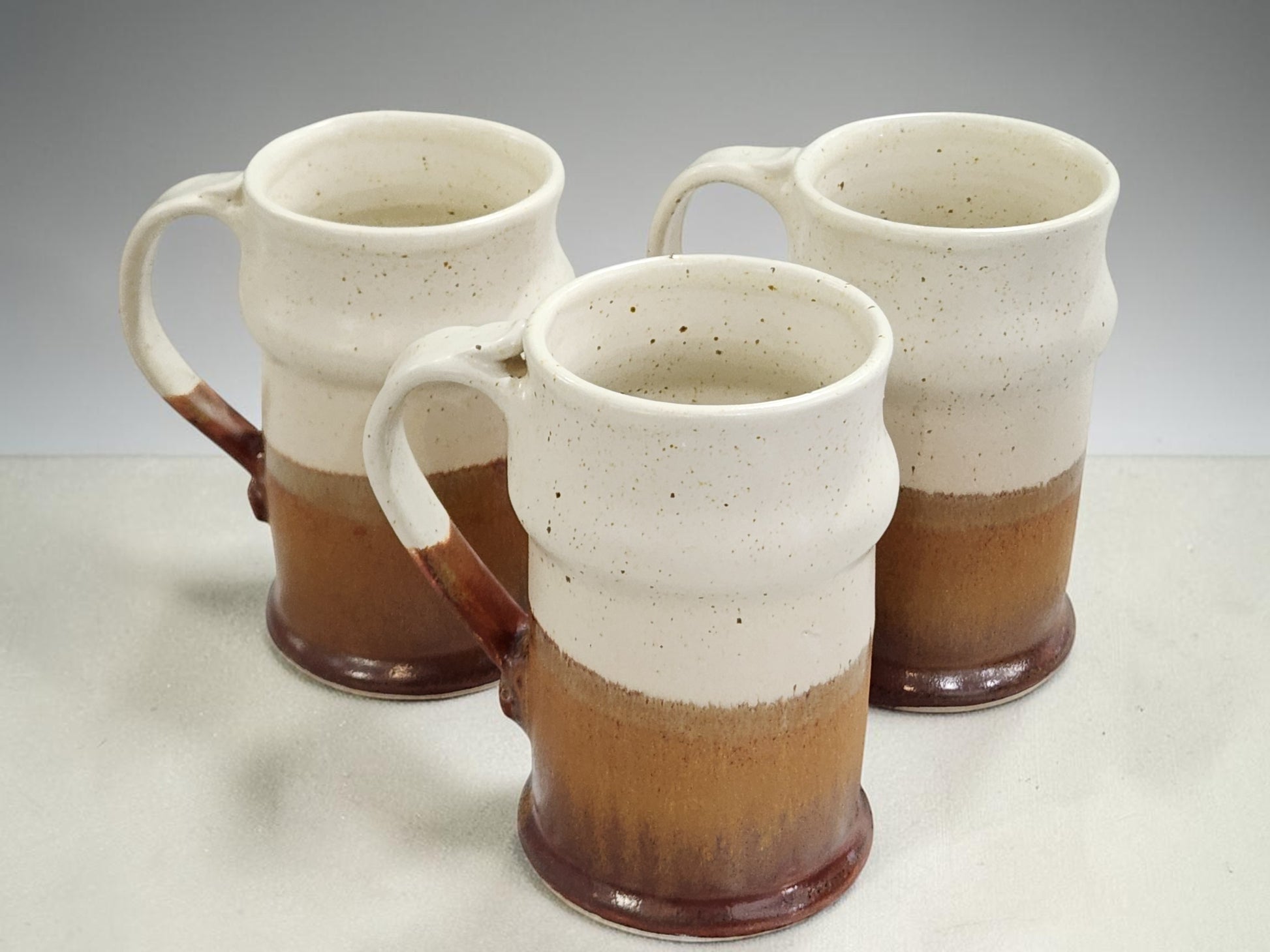 Set of three tall handmade pottery steins with speckled glaze and curved handles