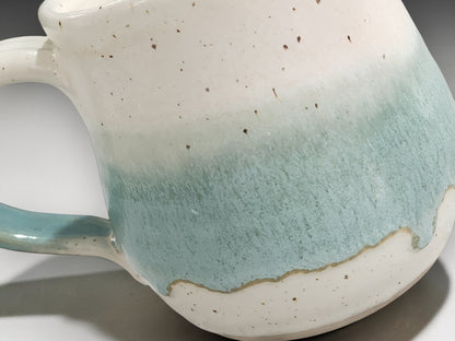 Close-up of speckled cream and soft green glaze on a handmade pottery mug