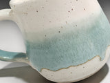 Close-up of speckled cream and soft green glaze on a handmade pottery mug