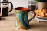 Handmade pottery mug on wooden bench with French press coffee scene