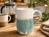 Handmade cream and green pottery mug styled on a timber bench with coffee setting