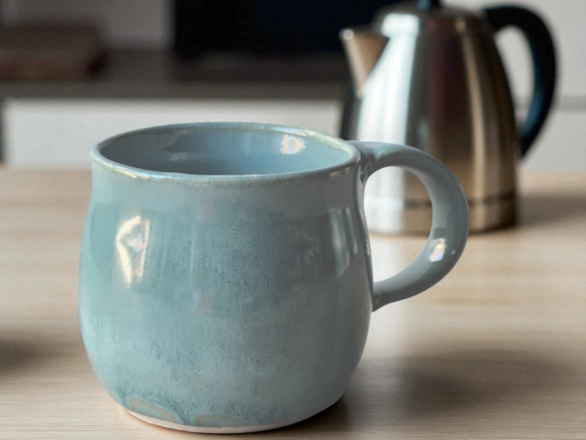 Blue ceramic mug on a wooden surface with a coffee pot in the  background