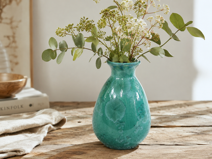 Green crystalline porcelain vase with foliage and white flowers on a timber table