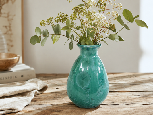 Green crystalline porcelain vase with foliage and white flowers on a timber table
