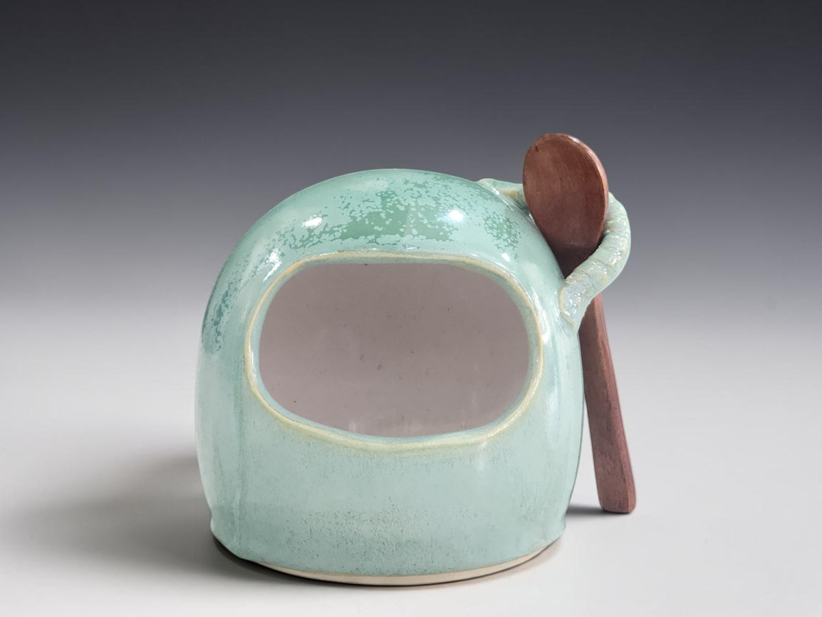 Mottled green ceramic salt cellar filled with coarse sea salt on a timber bench