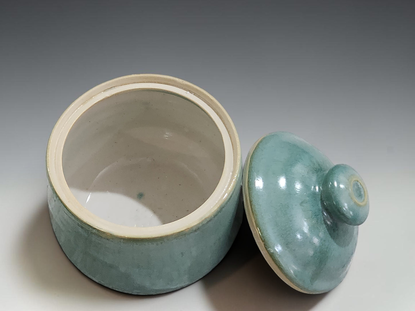 Handmade ceramic sugar bowl on grey studio background showing lidded form and seafoam glaze