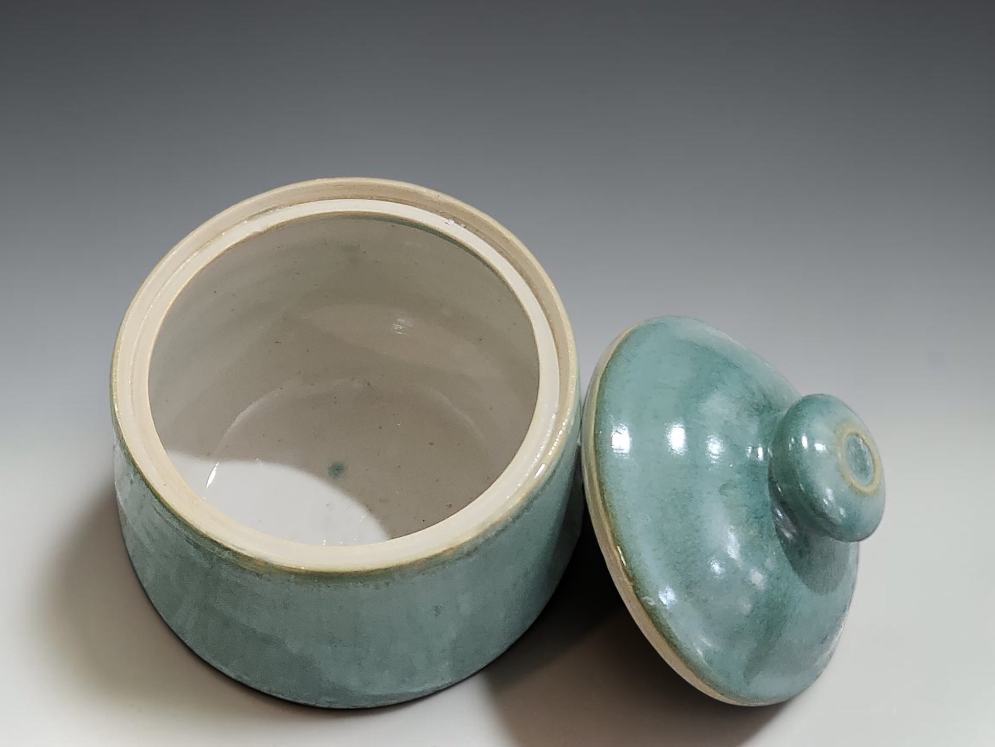Handmade ceramic sugar bowl on grey studio background showing lidded form and seafoam glaze